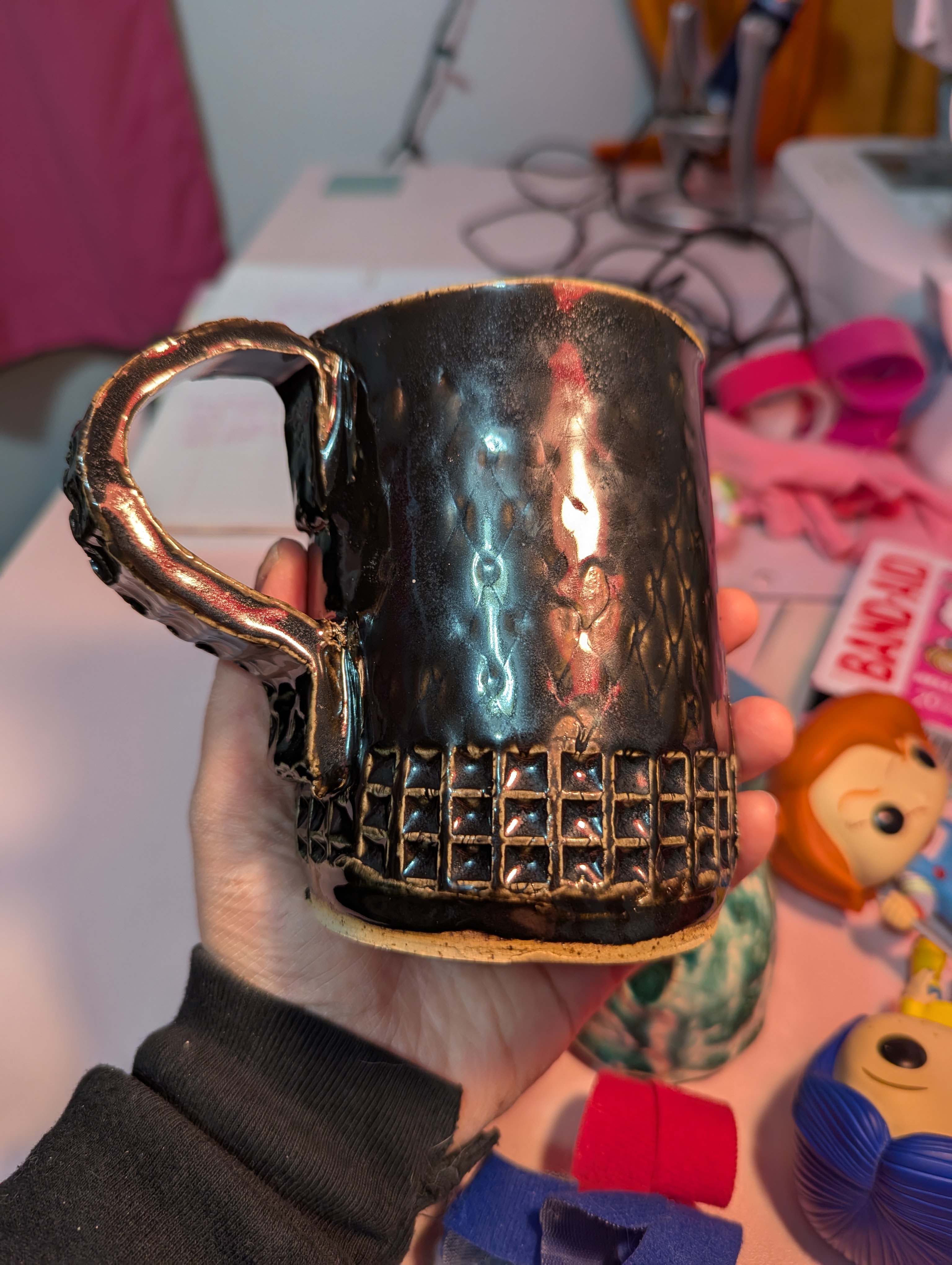 Side of a handbuilt mug with stud and fishnet texture and ebony glaze.
